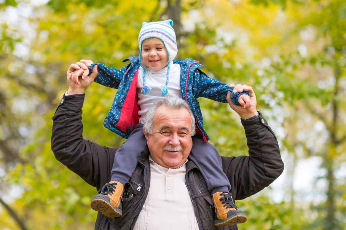 Grandfather carrying a smiling child on his shoulders outdoors, representing an active life after shoulder replacement